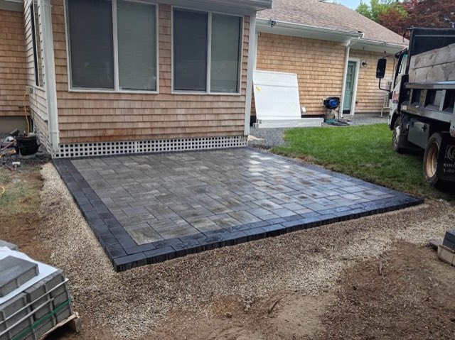 New gray paver patio with a dark border behind a shingled home