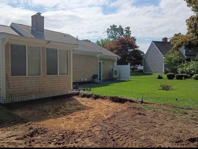 Bare dirt area behind a shingled home before a new patio was built